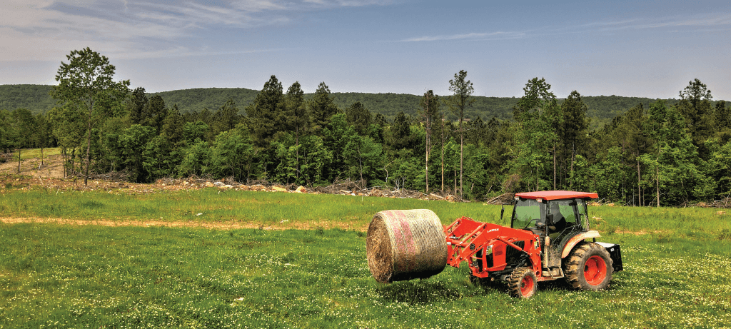 Tractor carrying a bale of hay in a field
